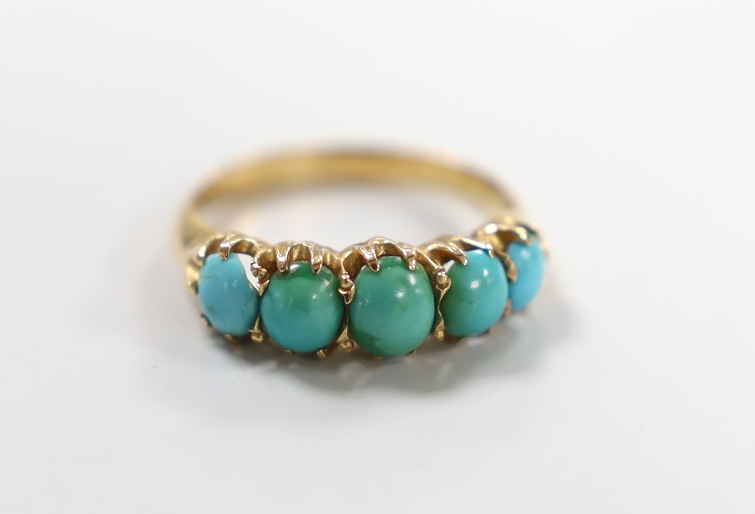 A yellow metal and graduated five stone cabochon turquoise set half hoop ring, size G/H, gross weight 2.4 grams.